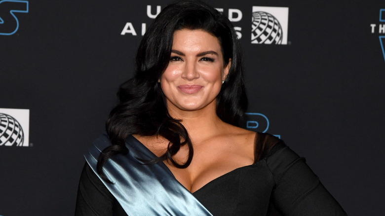 Gina Carano wearing a black long-sleeved dress with a blue satin sash