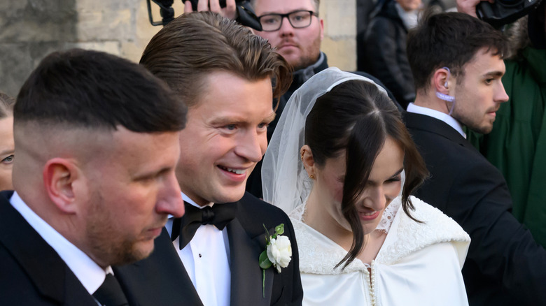 Adam Peaty and Holly Ramsay gaze downward while smiling and walking on their wedding day.