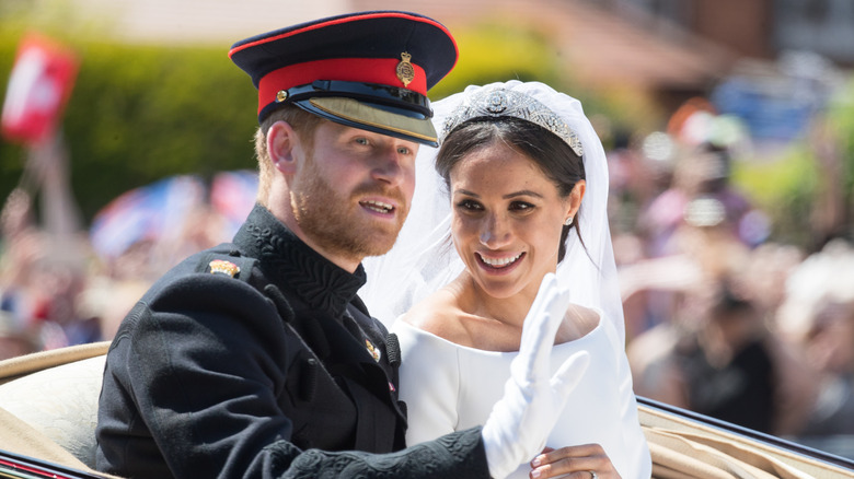 Meghan Markle smiles at Prince Harry, who is waving at the crowd.
