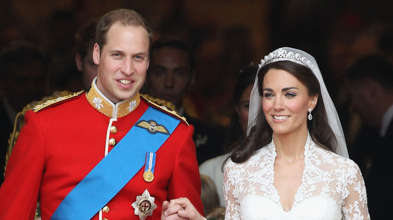 Prince William and Kate Middleton smile while holding hands at their wedding.