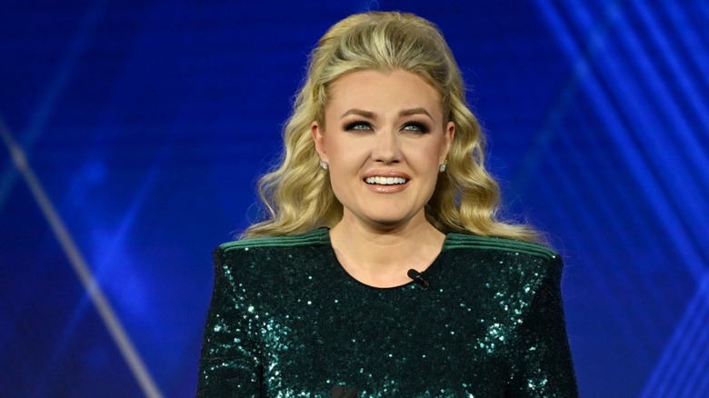 Wearing thick makeup and a smokey eye, Erika Kirk smiles while gazing upward.