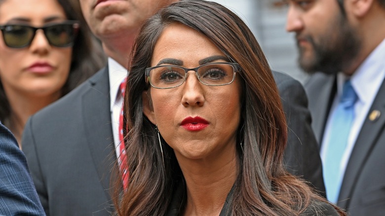 Wearing piled-on makeup and her signature red lipstick, Lauren Boebert stares directly at the camera.