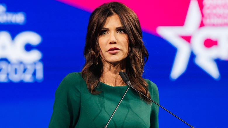 Kristi Noem wearing dark pink lipstick and a green dress at CPAC 2021.