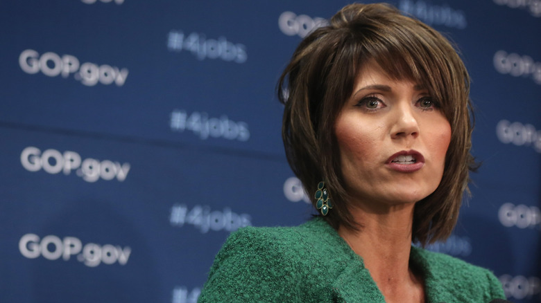 Kristi Noem wears her hair styled in a shaggy bobby and sports bright blush and berry lipstick while addressing the media in 2014.
