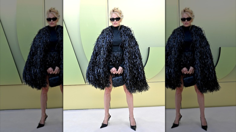 Pamela Anderson standing in all black at the Versace show in 2023.