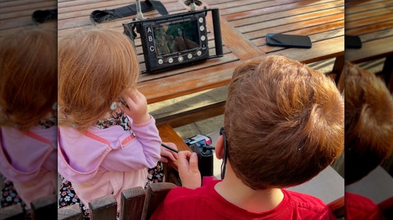 Lilibet and Archie watch Meghan Markle on a screen.