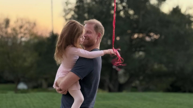 Prince Harry holds Lilibet with red balloons in her hand.