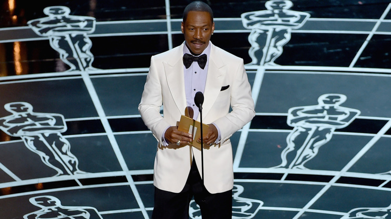 Eddie Murphy standing on Oscars stage in 2015 with an envelope