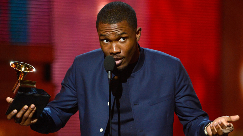Frank Ocean holding a Grammy award while giving an acceptance speech on stage with his hands out