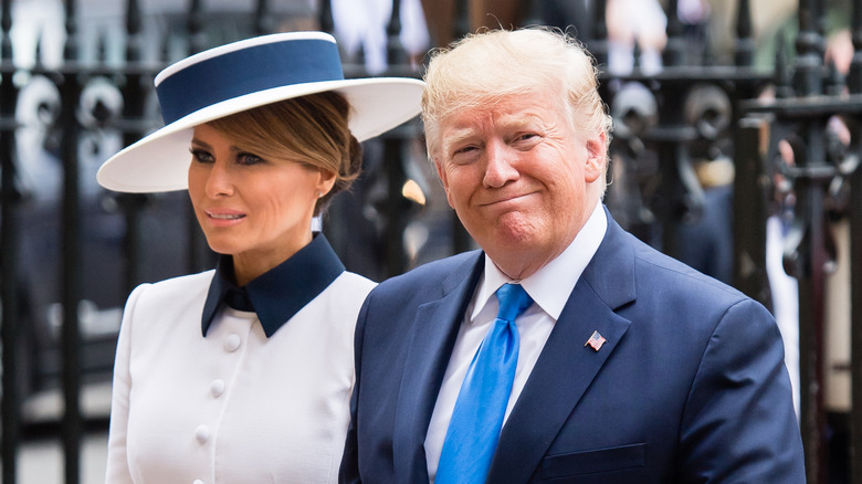 Melania Trump wearing a slanted white hat beside Donald Trump
