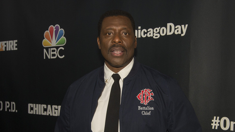 Eamonn Walker posing in Battalion Chief jacket, shirt and tie in front of ChicagoDay backdrop