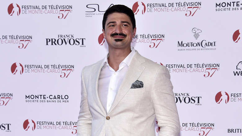 Yuriy Sardarov smiling in cream suit in front of backdrop