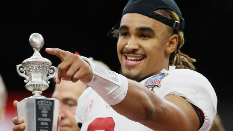 Jalen Hurts holds trophy while pointing and smiling