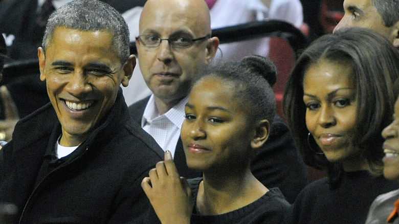 Sasha Obama smiles, wearing her hair in a bun and glossy lips.