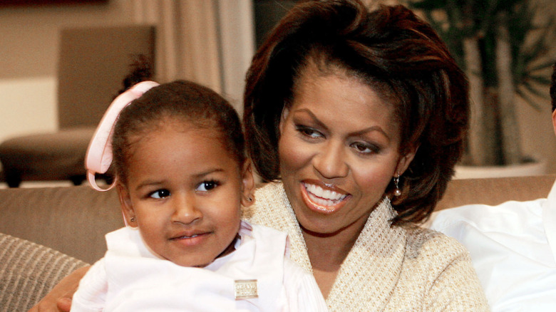 Michelle Obama is seen carrying a young Sasha Obama, who wears a pink hair accessory.