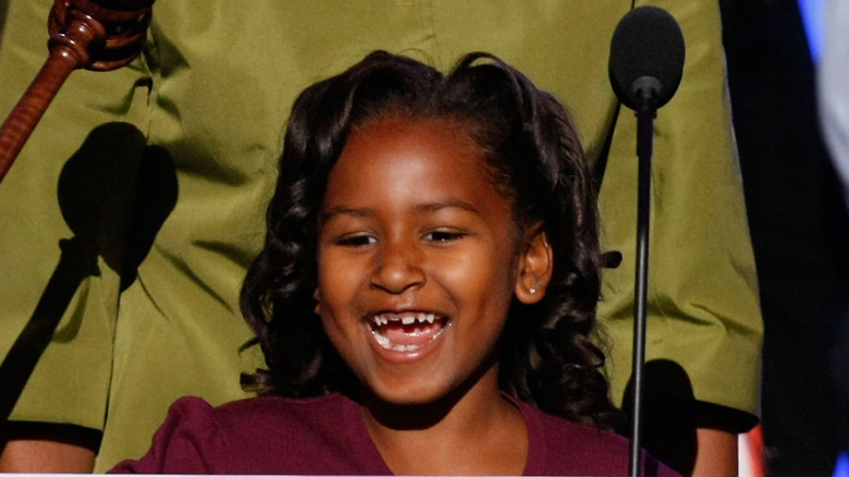 A young Sasha Obama with curly hair displays a toothy smile.