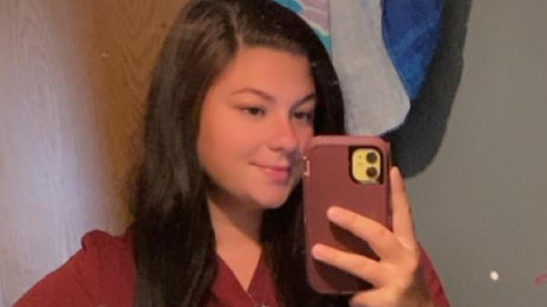 Sporting slightly wavy hair and a burgundy top, Autumn Crittendon takes a mirror selfie.