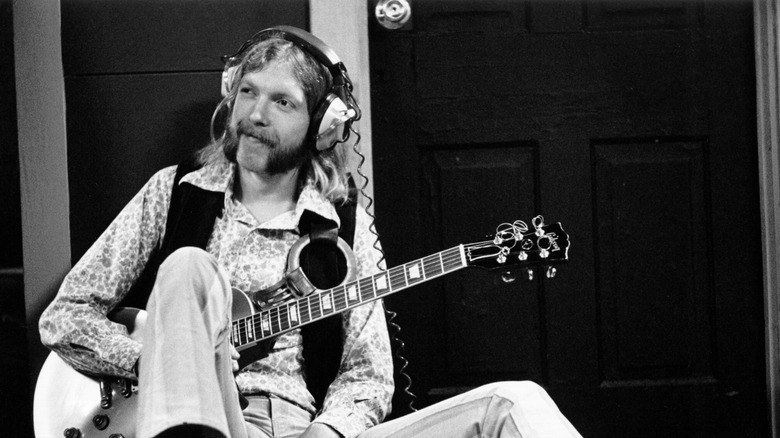 Duane Allman wearing headphones while holding a guitar