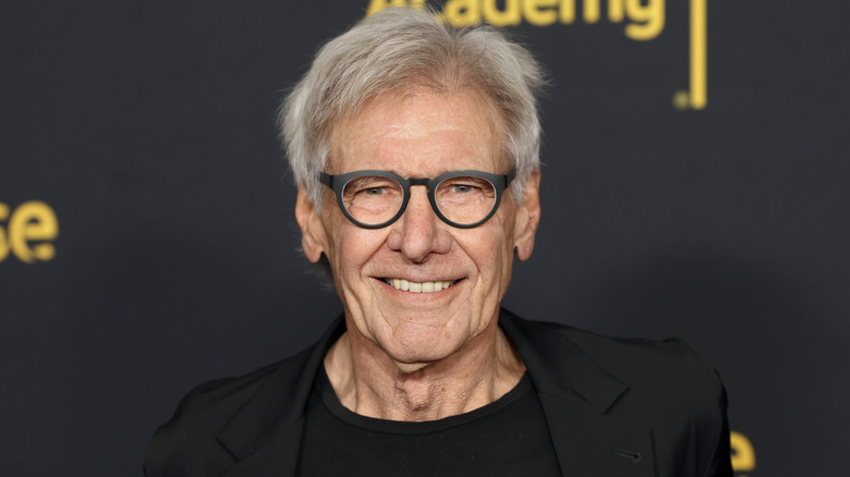 Harrison Ford wearing glasses and smiling in an all-black outfit