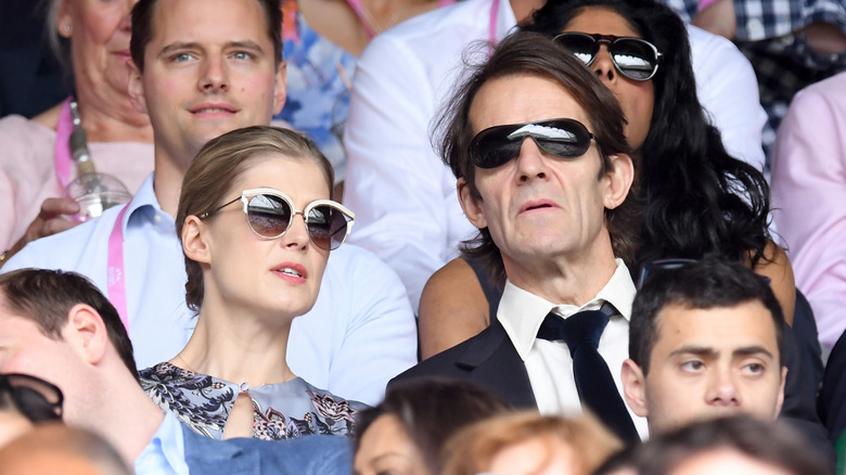 Rosamund Pike and Robie Uniacke wearing sunglasses and sitting together in a crowd.