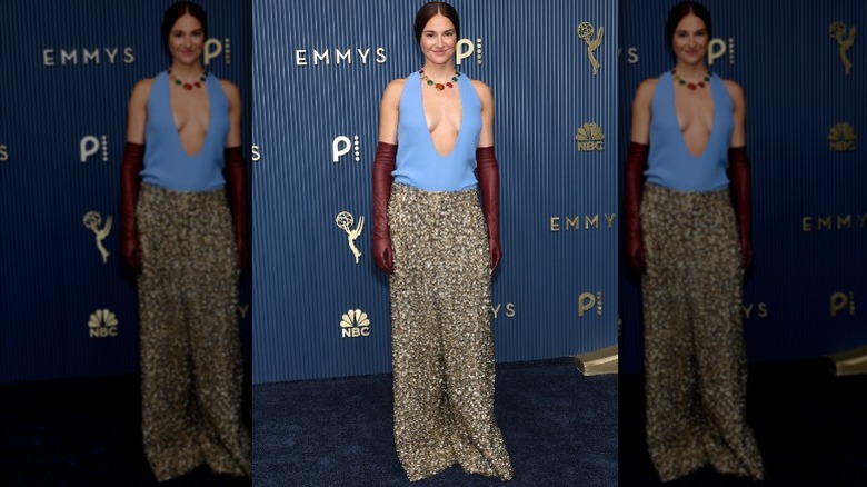 Shailene Woodley wearing red gloves, a blue top, and a gold skirt.