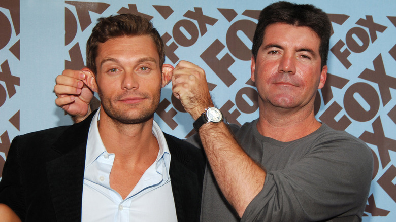 Simon Cowell playing with Ryan Seacrest's ears while they pose on the red carpet.