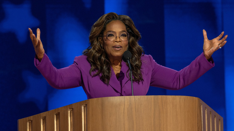 Oprah speaking to a crowd with her arms upraised.