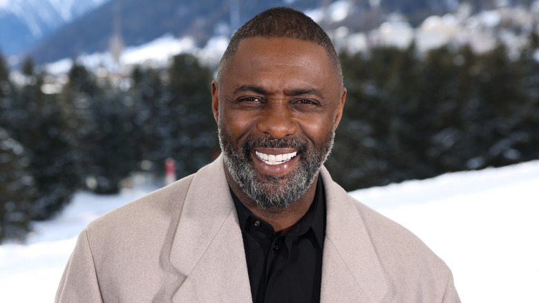 Idris Alba smiling in front of a mountain