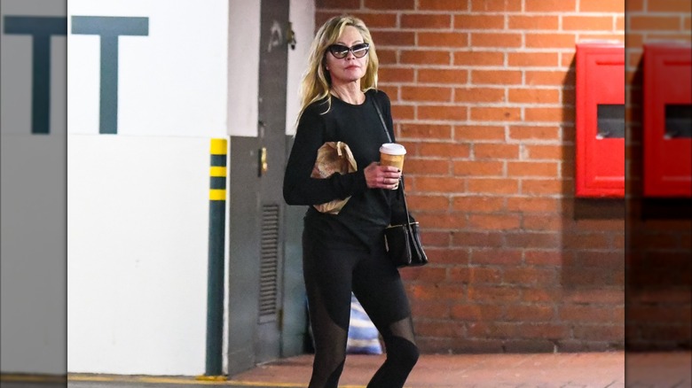 Melanie Griffith walking in workout gear with coffee.