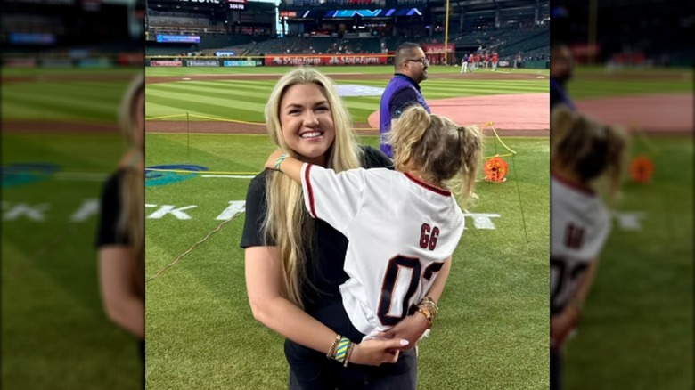 Erika Kirk holding her daughter on a baseball field.