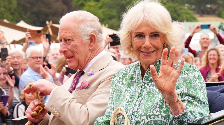 Queen Camilla waving while riding with Charles in a carriage