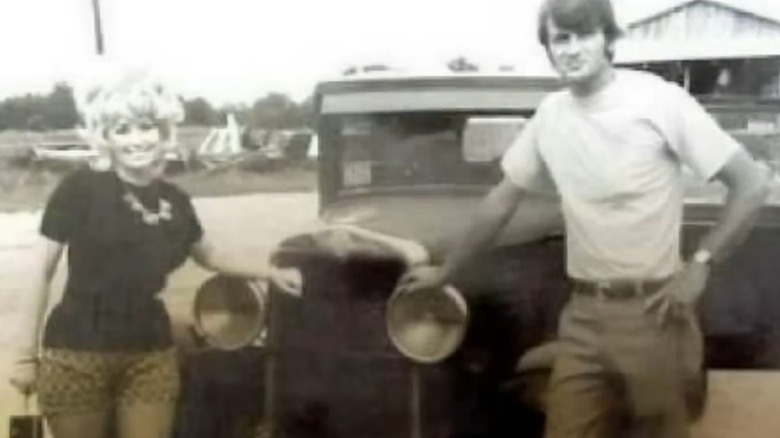 Dolly Parton and Carl Dean posing with a car.