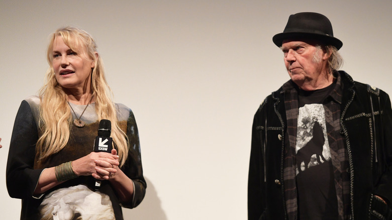 Darryl Hannah holds a microphone and looks to the side as Neil Young looks at her.