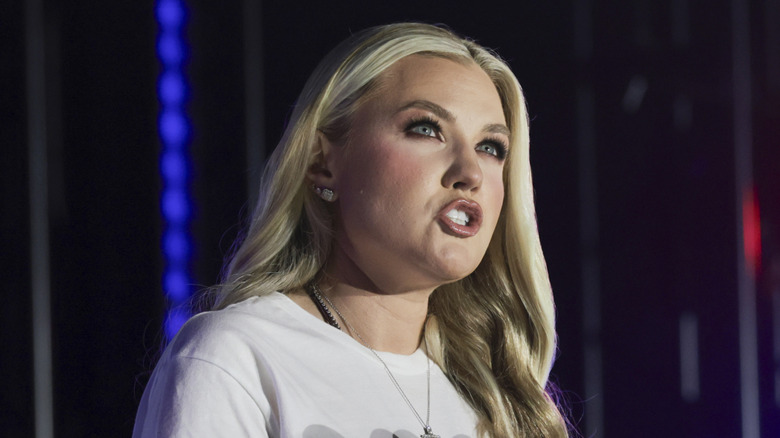 Erika Kirk speaking on stage at a Turning Point USA event in a white T-shirt