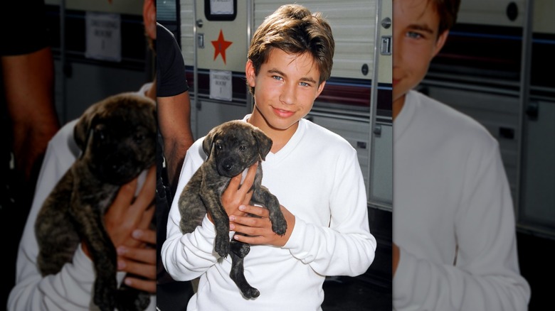 A young Jonathan Taylor Thomas holding a black puppy in front of a trailer.