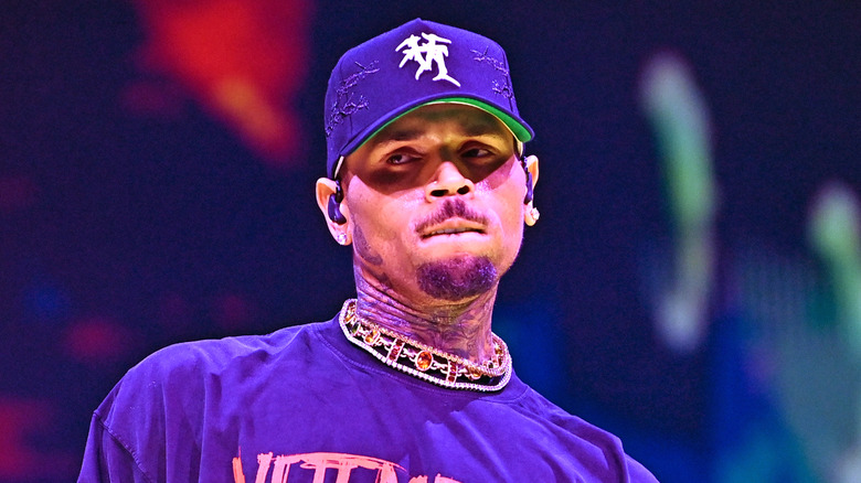 Chris Brown performing on stage wearing a blue t-shirt, blue hat and gold and beaded choker