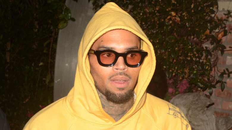 Chris Brown wearing thick black-rimmed glasses and a yellow hoodie