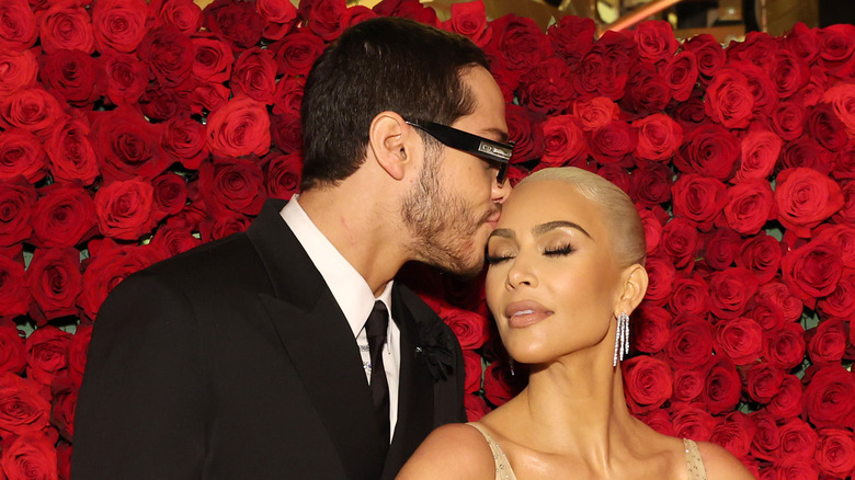 Pete Davidson kisses Kim Kardashian's forehead at an event, backdrop of roses