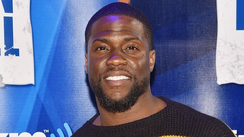 Kevin Hart wearing a black-and-yellow striped sweater, smiling at an event