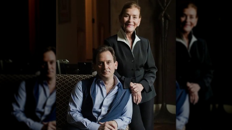 Adam Levy sitting with his mom smiling behind him.