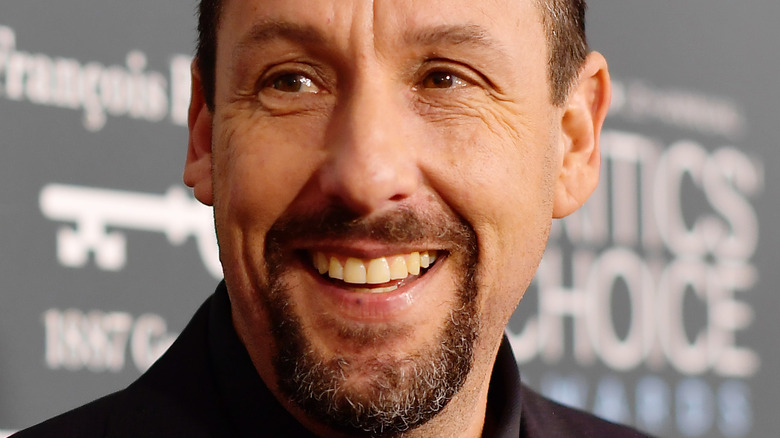 Adam Sandler smiles in a black suit