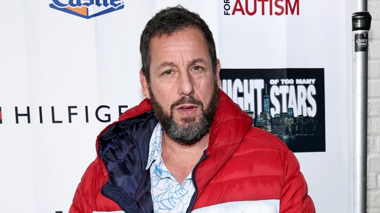Adam Sandler with a beard wearing a puffer jacket