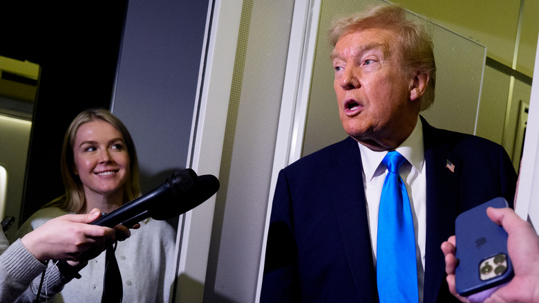 Donald Trump speaks to reporters as Karoline Leavitt smiles at him.