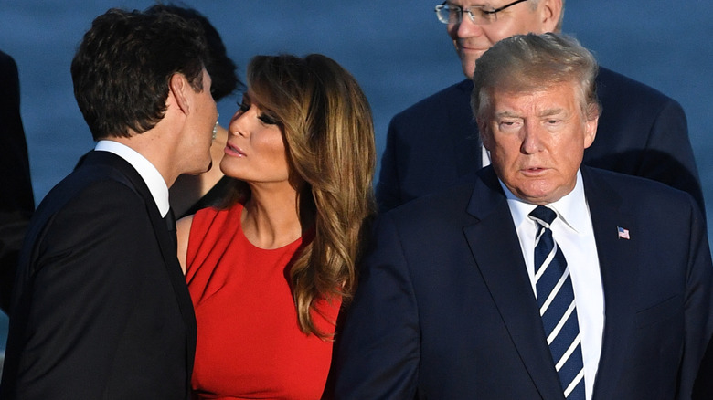 Melania Trump smiling leaning forward to kiss Justin Trudeau on the cheek as Donald Trump stands beside her.