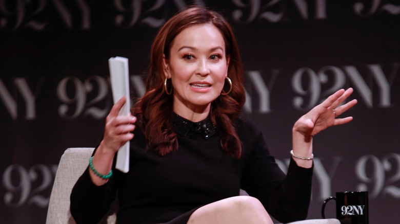 Eva Pilgrim gesturing while speaking on stage at 92NY in a black long-sleeved dress and hoop earrings