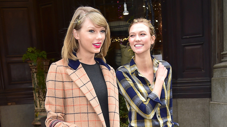 Taylor Swift walking with Karlie Kloss, who is smiling at Swift