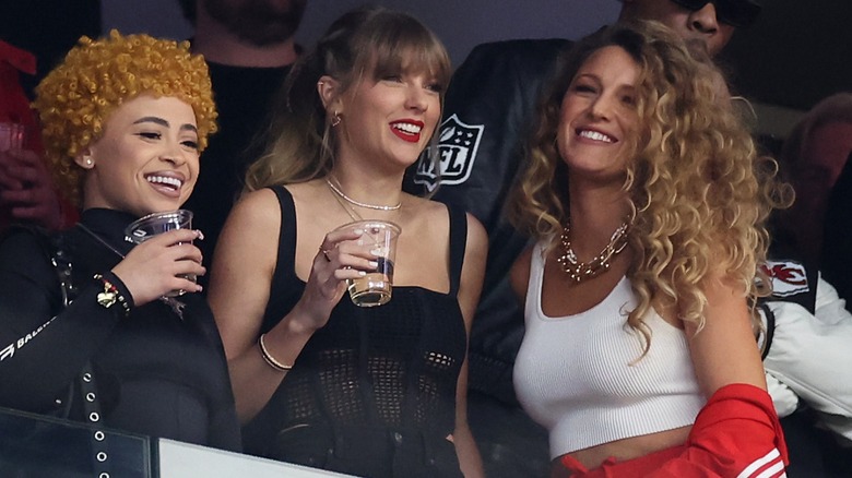 Taylor Swift and Ice Spice laugh as they hold drinks in cups, while Blake Lively also laughs along.
