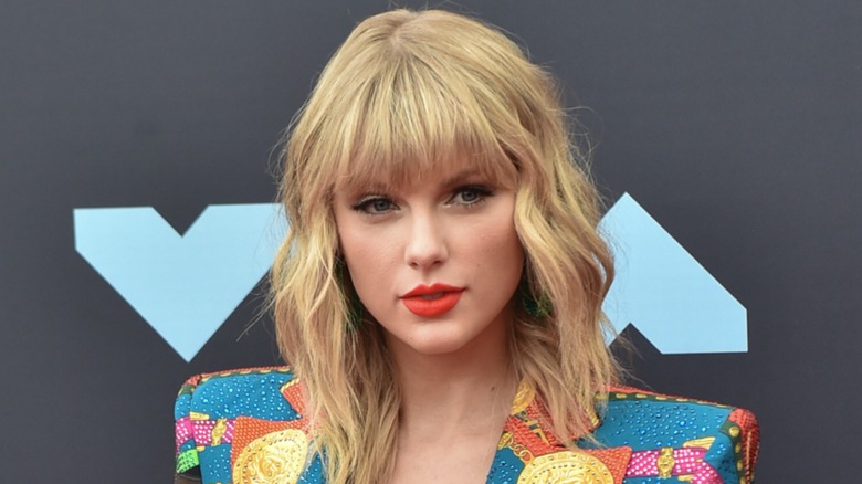 Sporting a multi-colored coat, Taylor Swift delivers an innocent-looking facial expression on the red carpet.