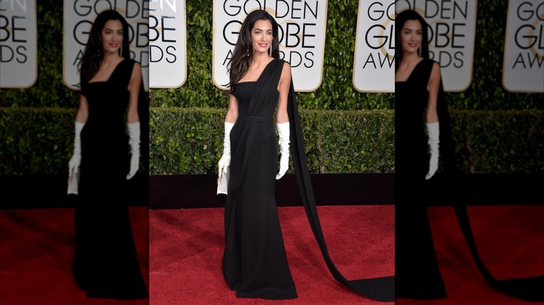 Amal posing on the red carpet at the Golden Globes wearing black gown and white gloves
