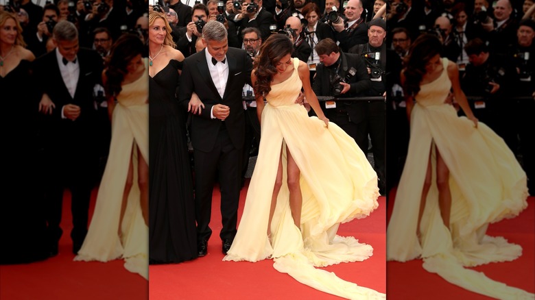 Amal fixing her gown on the red carpet beside George Clooney